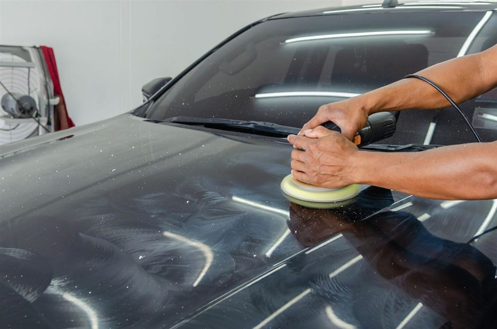 Dual-action polisher refining a glossy black hood